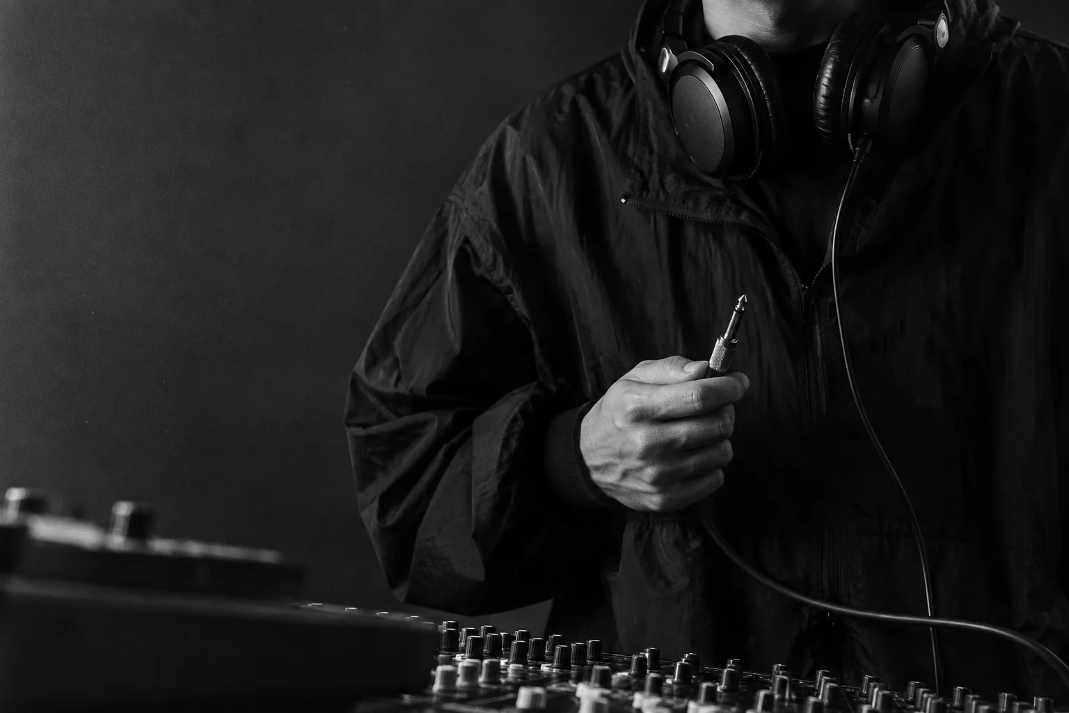 Productor con audífonos sosteniendo un cable frente a una consola de sonido, en blanco y negro